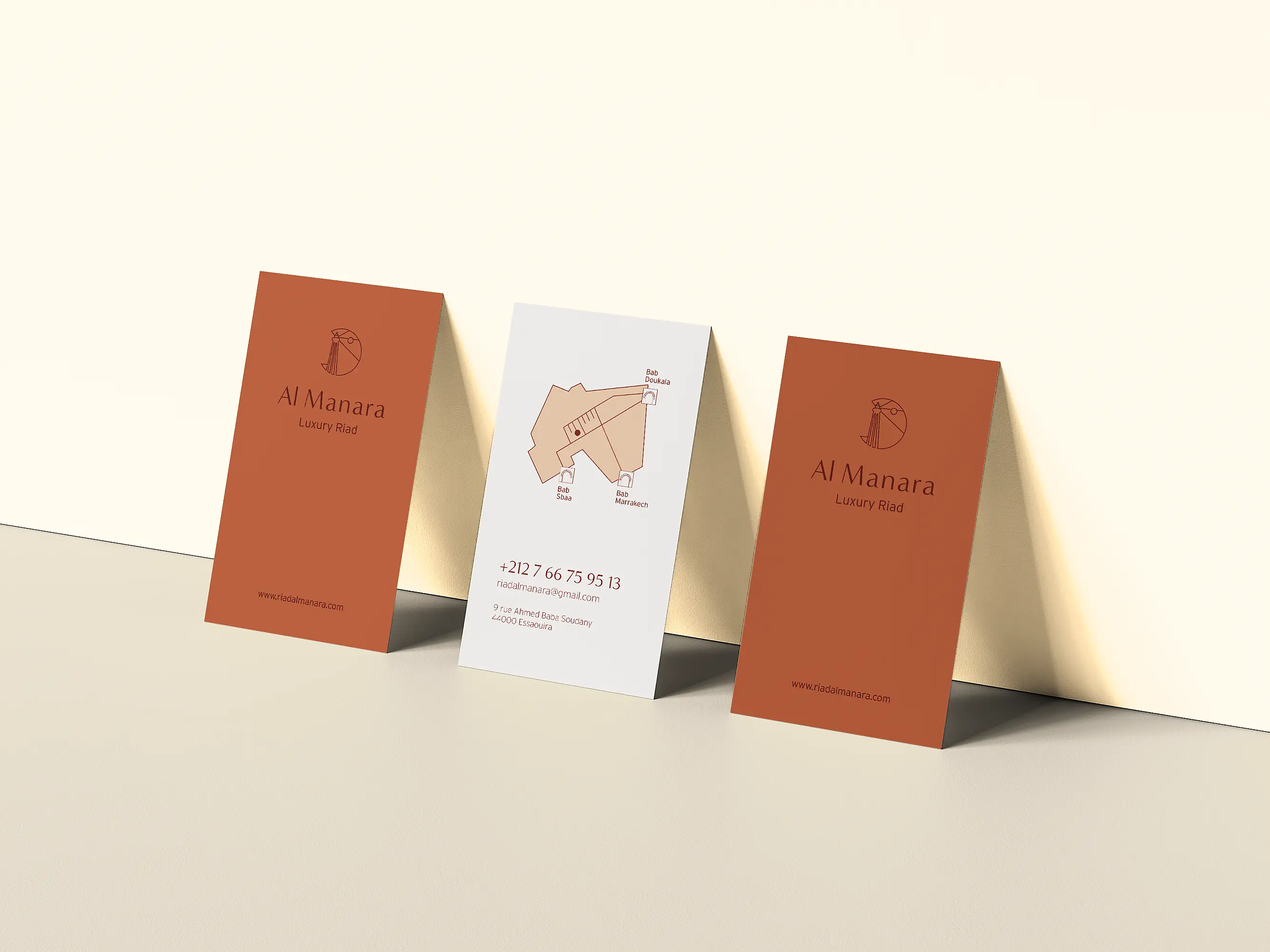 Des cartes de visite recto-verso apposées contre un mur présentent le logo Al Manara sur fond marron et un plan sur fond blanc.